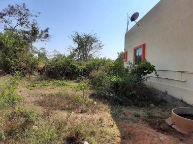 Bangalore, Karnataka, Hindistan-07-2021: Satılık boş bir arazinin güzel manzarası ve ormanda yeni inşa edilmiş bir evin yanı