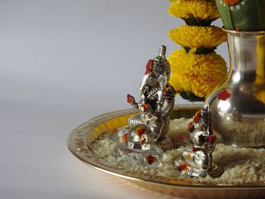 Kasımpatı çiçeği, yaprak, hindistancevizi, kumkum ve zerdeçal ile süslenmiş gümüş kalaş kapağı beyaz arka planda izole edilmiş bir tabakta Ganesha, lakshmi ve shivalinga heykeli.