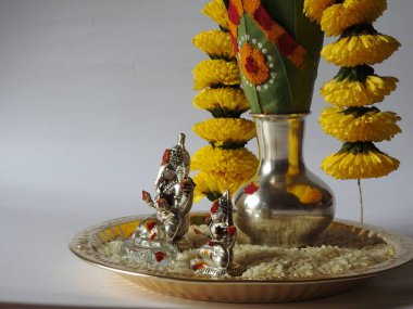 Kasımpatı çiçeği, yaprak, hindistancevizi, kumkum ve zerdeçal ile süslenmiş gümüş kalaş kapağı beyaz arka planda izole edilmiş bir tabakta Ganesha, lakshmi ve shivalinga heykeli.