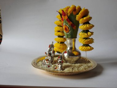 Kasımpatı çiçeği, yaprak, hindistancevizi, kumkum ve zerdeçal ile süslenmiş gümüş kalaş kapağı beyaz arka planda izole edilmiş bir tabakta Ganesha, lakshmi ve shivalinga heykeli.