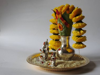 Kasımpatı çiçeği, yaprak, hindistancevizi, kumkum ve zerdeçal ile süslenmiş gümüş kalaş kapağı beyaz arka planda izole edilmiş bir tabakta Ganesha, lakshmi ve shivalinga heykeli.