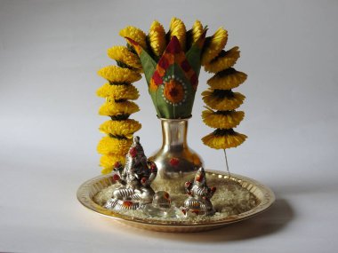 Kasımpatı çiçeği, yaprak, hindistancevizi, kumkum ve zerdeçal ile süslenmiş gümüş kalaş kapağı beyaz arka planda izole edilmiş bir tabakta Ganesha, lakshmi ve shivalinga heykeli.