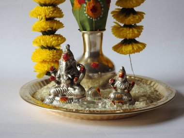 Kasımpatı çiçeği, yaprak, hindistancevizi, kumkum ve zerdeçal ile süslenmiş gümüş kalaş kapağı beyaz arka planda izole edilmiş bir tabakta Ganesha, lakshmi ve shivalinga heykeli.