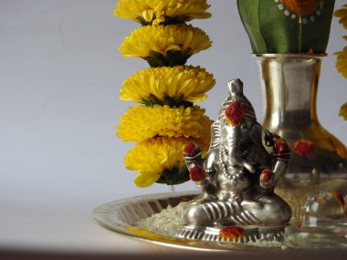 Kasımpatı çiçeği, yaprak, hindistancevizi, kumkum ve zerdeçal ile süslenmiş gümüş kalaş kapağı beyaz arka planda izole edilmiş bir tabakta Ganesha, lakshmi ve shivalinga heykeli.