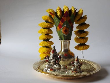 Kasımpatı çiçeği, yaprak, hindistancevizi, kumkum ve zerdeçal ile süslenmiş gümüş kalaş kapağı beyaz arka planda izole edilmiş bir tabakta Ganesha, lakshmi ve shivalinga heykeli.