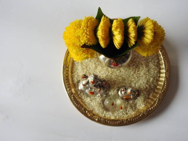 Kasımpatı çiçeği, yaprak, hindistancevizi, kumkum ve zerdeçal ile süslenmiş gümüş kalaş kapağı beyaz arka planda izole edilmiş bir tabakta Ganesha, lakshmi ve shivalinga heykeli.