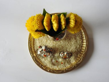 Kasımpatı çiçeği, yaprak, hindistancevizi, kumkum ve zerdeçal ile süslenmiş gümüş kalaş kapağı beyaz arka planda izole edilmiş bir tabakta Ganesha, lakshmi ve shivalinga heykeli.