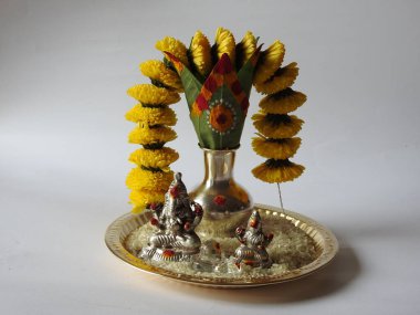 Kasımpatı çiçeği, yaprak, hindistancevizi, kumkum ve zerdeçal ile süslenmiş gümüş kalaş kapağı beyaz arka planda izole edilmiş bir tabakta Ganesha, lakshmi ve shivalinga heykeli.