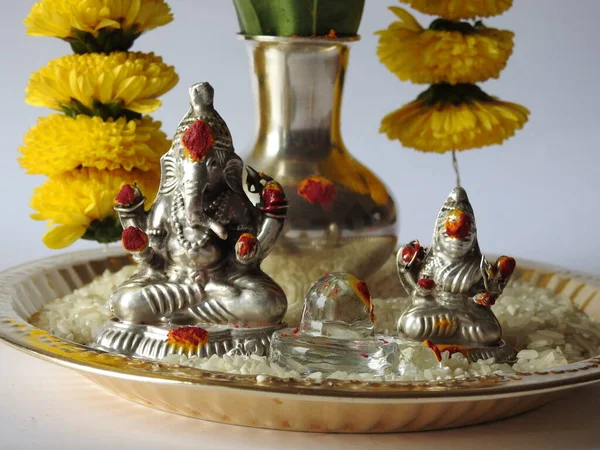 Kasımpatı çiçeği, yaprak, hindistancevizi, kumkum ve zerdeçal ile süslenmiş gümüş kalaş kapağı beyaz arka planda izole edilmiş bir tabakta Ganesha, lakshmi ve shivalinga heykeli.