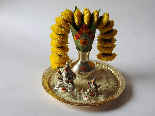 Kasımpatı çiçeği, yaprak, hindistancevizi, kumkum ve zerdeçal ile süslenmiş gümüş kalaş kapağı beyaz arka planda izole edilmiş bir tabakta Ganesha, lakshmi ve shivalinga heykeli.