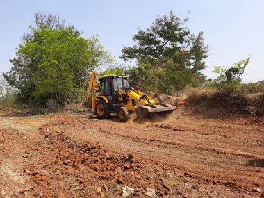 Bangalore, Karnataka, India-Mar 21 2021: Closeup of JCB cleaning land for construction of building at forest or countryside