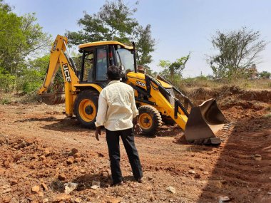 Bangalore, Karnataka, India-Mar 21 2021: Closeup of JCB cleaning land for construction of building at forest or countryside