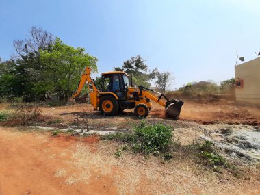 Bangalore, Karnataka, India-Mar 21 2021: Closeup of JCB cleaning land for construction of building at forest or countryside