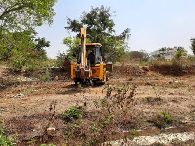 Bangalore, Karnataka, India-Mar 21 2021: Closeup of JCB cleaning land for construction of building at forest or countryside