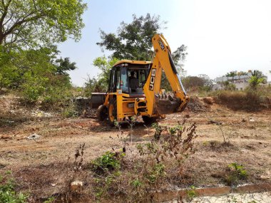 Bangalore, Karnataka, India-Mar 21 2021: Closeup of JCB cleaning land for construction of building at forest or countryside
