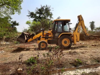 Bangalore, Karnataka, India-Mar 21 2021: Closeup of JCB cleaning land for construction of building at forest or countryside