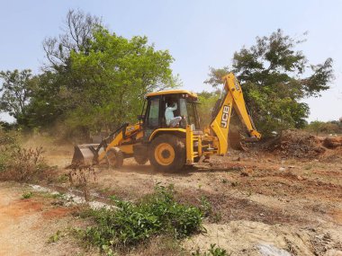 Bangalore, Karnataka, India-Mar 21 2021: Closeup of JCB cleaning land for construction of building at forest or countryside