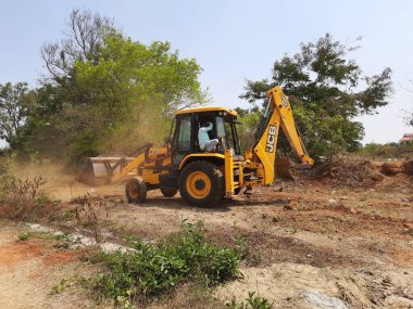 Bangalore, Karnataka, India-Mar 21 2021: Closeup of JCB cleaning land for construction of building at forest or countryside