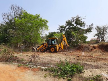 Bangalore, Karnataka, India-Mar 21 2021: Closeup of JCB cleaning land for construction of building at forest or countryside