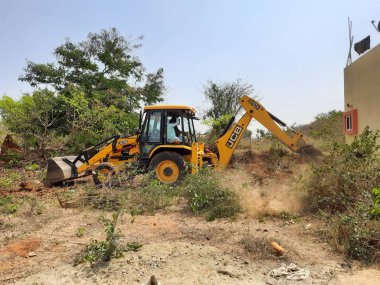 Bangalore, Karnataka, India-Mar 21 2021: Closeup of JCB cleaning land for construction of building at forest or countryside