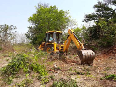 Bangalore, Karnataka, India-Mar 21 2021: Closeup of JCB cleaning land for construction of building at forest or countryside
