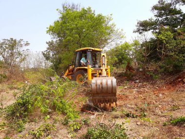 Bangalore, Karnataka, India-Mar 21 2021: Closeup of JCB cleaning land for construction of building at forest or countryside