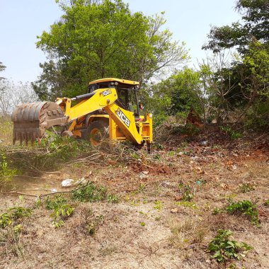 Bangalore, Karnataka, India-Mar 21 2021: Closeup of JCB cleaning land for construction of building at forest or countryside