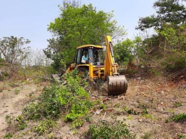 Bangalore, Karnataka, India-Mar 21 2021: Closeup of JCB cleaning land for construction of building at forest or countryside