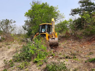 Bangalore, Karnataka, India-Mar 21 2021: Closeup of JCB cleaning land for construction of building at forest or countryside