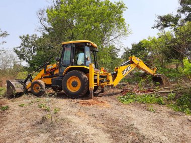 Bangalore, Karnataka, India-Mar 21 2021: Closeup of JCB cleaning land for construction of building at forest or countryside