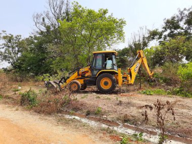 Bangalore, Karnataka, India-Mar 21 2021: Closeup of JCB cleaning land for construction of building at forest or countryside