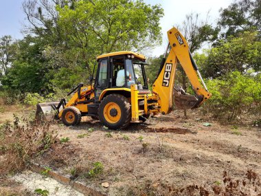 Bangalore, Karnataka, India-Mar 21 2021: Closeup of JCB cleaning land for construction of building at forest or countryside