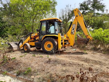 Bangalore, Karnataka, India-Mar 21 2021: Closeup of JCB cleaning land for construction of building at forest or countryside