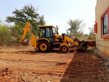 Bangalore, Karnataka, India-Mar 21 2021: Closeup of JCB cleaning land for construction of building at forest or countryside