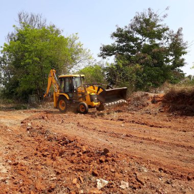 Bangalore, Karnataka, India-Mar 21 2021: Closeup of JCB cleaning land for construction of building at forest or countryside
