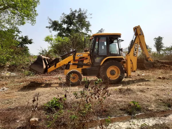 Bangalore, Karnataka, India-Mar 21 2021: Closeup of JCB cleaning land for construction of building at forest or countryside