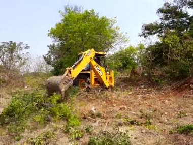 Bangalore, Karnataka, India-Mar 21 2021: Closeup of JCB cleaning land for construction of building at forest or countryside