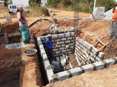 Bangalore, Karnataka, Hindistan-Nisan 10 2021: Hintli işçilerin yeni bina inşaatı, su kuyusu ve inşaat malzemelerini su kullanarak karıştırması.