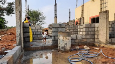 Bangalore, Karnataka, Hindistan-30 Nisan 2021: Yeni bina inşaatı ve temizlik evi gören Hintli genç anne ve çocuğun yakın çekimi