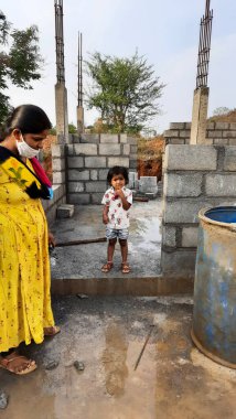 Bangalore, Karnataka, Hindistan-30 Nisan 2021: Yeni bina inşaatı ve temizlik evi gören Hintli genç anne ve çocuğun yakın çekimi