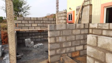 Bangalore, Karnataka, Hindistan-20 Nisan 2021: Yeni konut çimentosu duvar tuğlalarını doğa arka planında sütunlarla örüyor