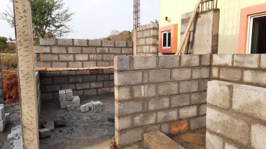 Bangalore, Karnataka, Hindistan-20 Nisan 2021: Yeni konut çimentosu duvar tuğlalarını doğa arka planında sütunlarla örüyor