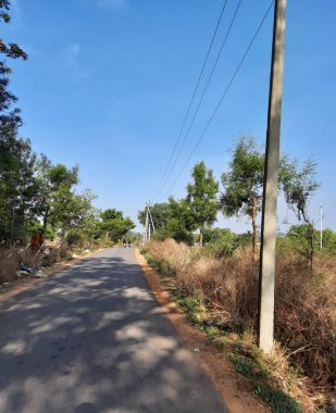 Bangalore, Karnataka, Hindistan-Mayıs 09 2021: Elektrik direği ve yolda ağaçların gölgesi olan güzel Bangalore Köy yollarının kapatılması. Bisiklet süren genç adam..