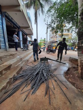 Bangalore, Karnataka, India-June 05 2021: Closeup of two indian young man wear mask and cutting the hexagon window rod manually in the road side during lockdown, covid 19 season