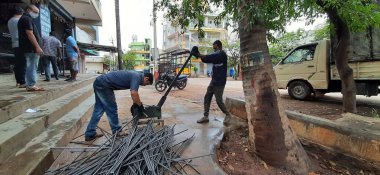 Bangalore, Karnataka, India-June 05 2021: Closeup of two indian young man wear mask and cutting the hexagon window rod manually in the road side during lockdown, covid 19 season