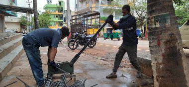 Bangalore, Karnataka, India-June 05 2021: Closeup of two indian young man wear mask and cutting the hexagon window rod manually in the road side during lockdown, covid 19 season