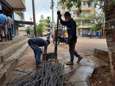 Bangalore, Karnataka, India-June 05 2021: Closeup of two indian young man wear mask and cutting the hexagon window rod manually in the road side during lockdown, covid 19 season