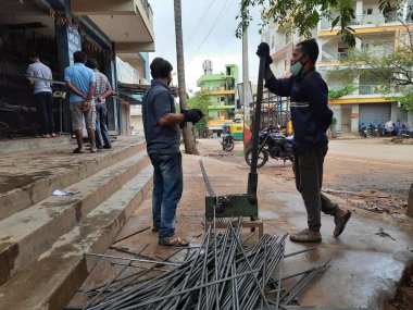 Bangalore, Karnataka, India-June 05 2021: Closeup of two indian young man wear mask and cutting the hexagon window rod manually in the road side during lockdown, covid 19 season