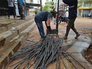 Bangalore, Karnataka, India-June 05 2021: Closeup of two indian young man wear mask and cutting the hexagon window rod manually in the road side during lockdown, covid 19 season