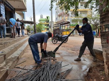 Bangalore, Karnataka, India-June 05 2021: Closeup of two indian young man wear mask and cutting the hexagon window rod manually in the road side during lockdown, covid 19 season